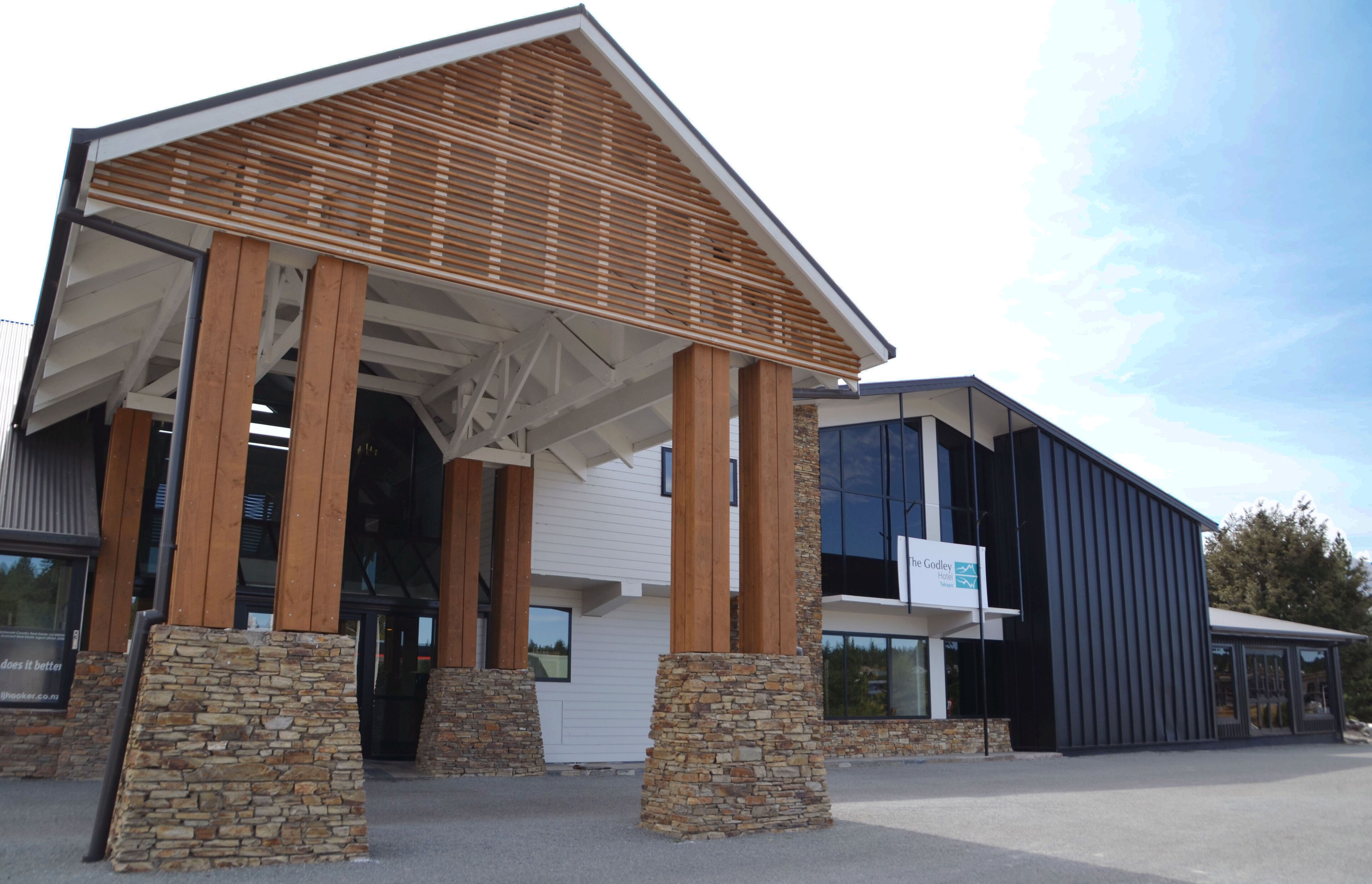 A modern building with a covered entrance, stone pillars, and a sign indicating a business.