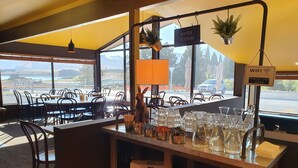 Un interior de restaurante con una zona de bar, distribución de mesas y vistas al exterior.