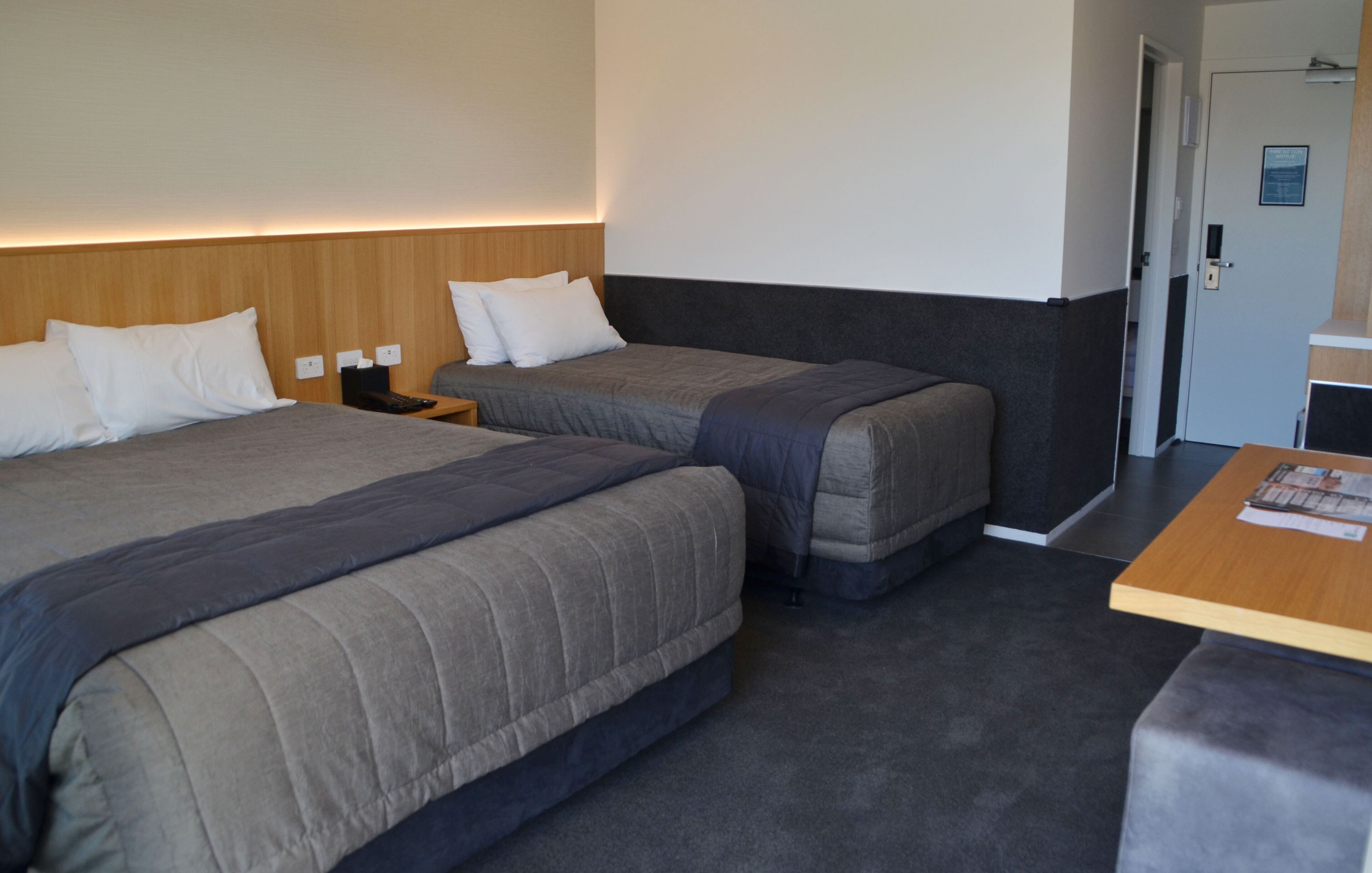 A hotel room with two beds, a wooden headboard, a small table, and a door.