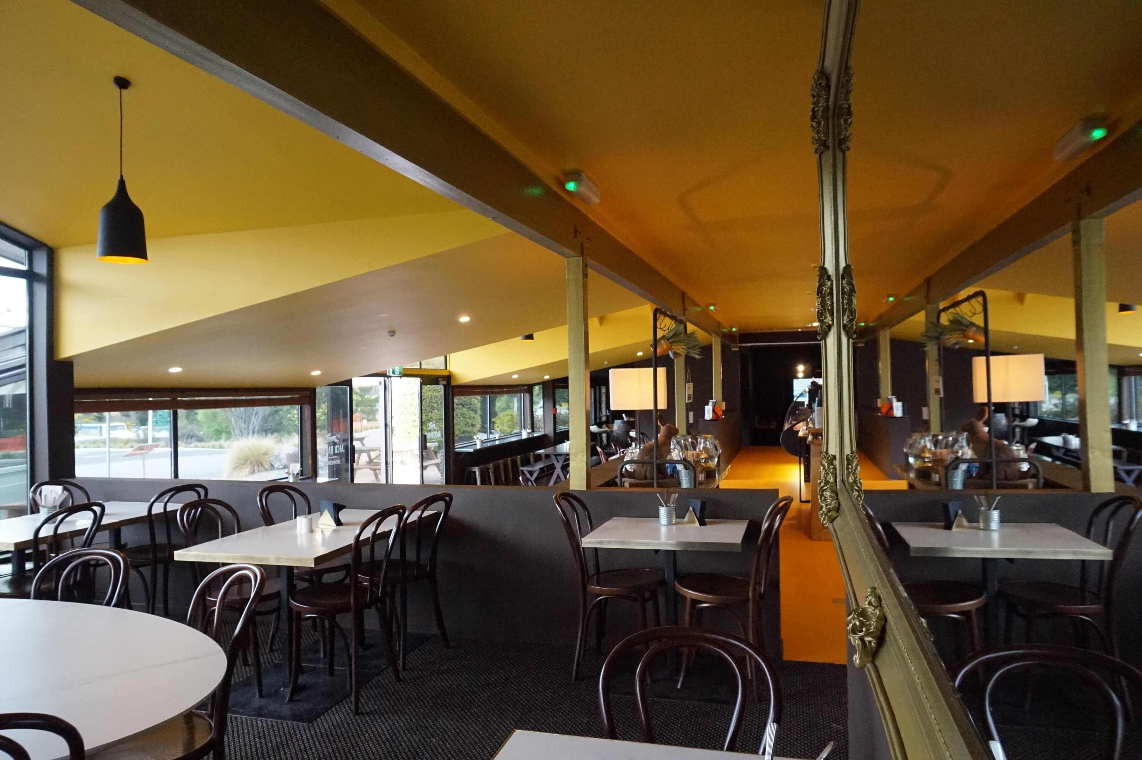 A restaurant with multiple tables and chairs, large windows, and a central walkway.