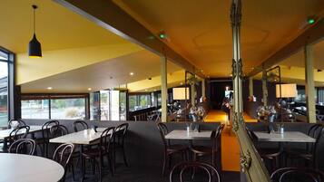 A restaurant with multiple tables and chairs, large windows, and a central walkway.