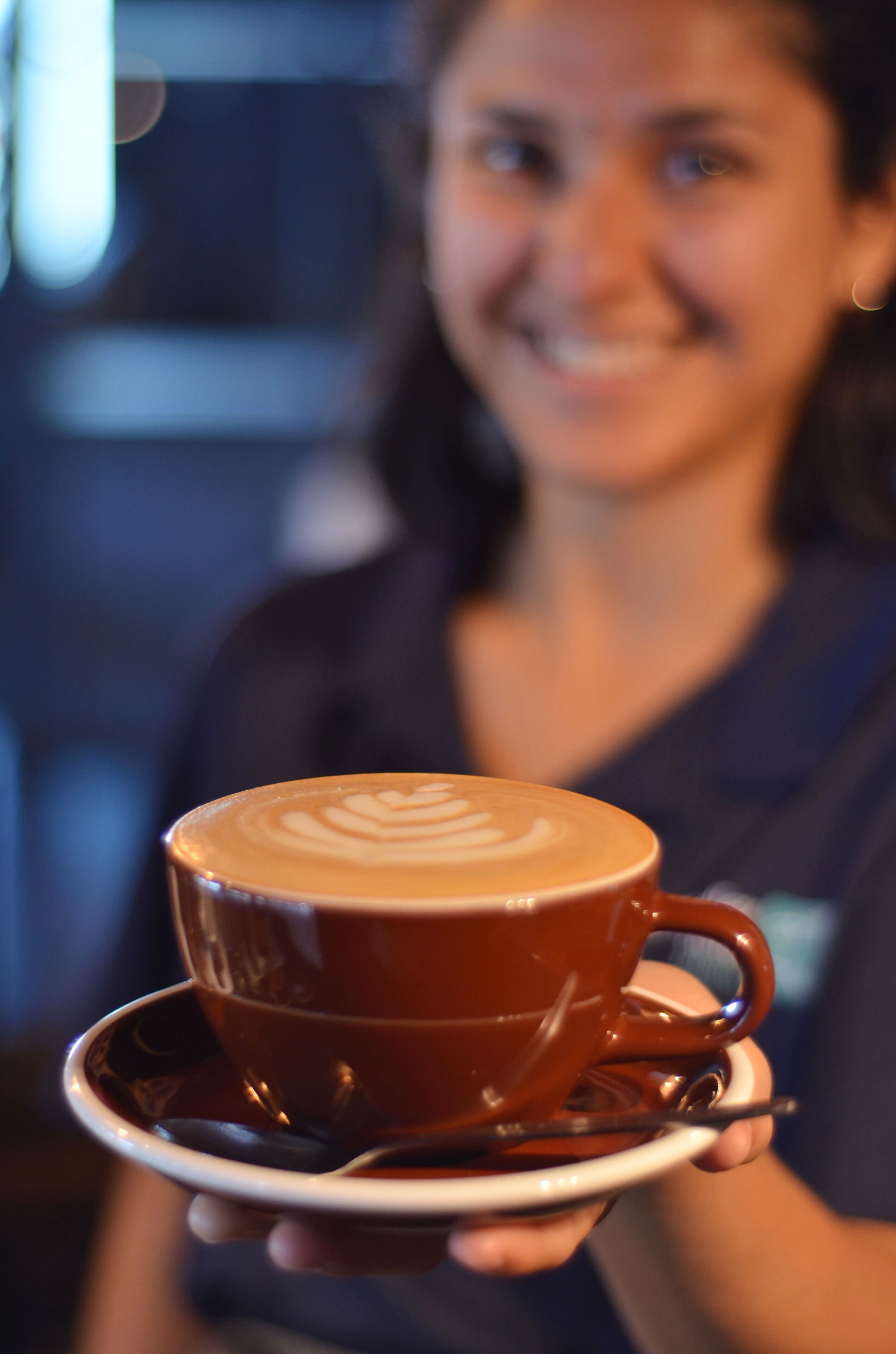 Eine Person hält eine Tasse Kaffee mit Latte-Art auf einem Untertasse.