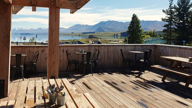 Una terraza de madera con mesas y sillas con vista a un lago y montañas.