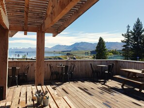 Une terrasse en bois, agrémentée de tables et de chaises, qui offre une vue sur un lac et des montagnes.