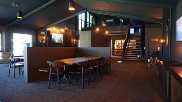 A spacious room with a high ceiling, a wooden table and chairs, and a staircase leading to an upper level.