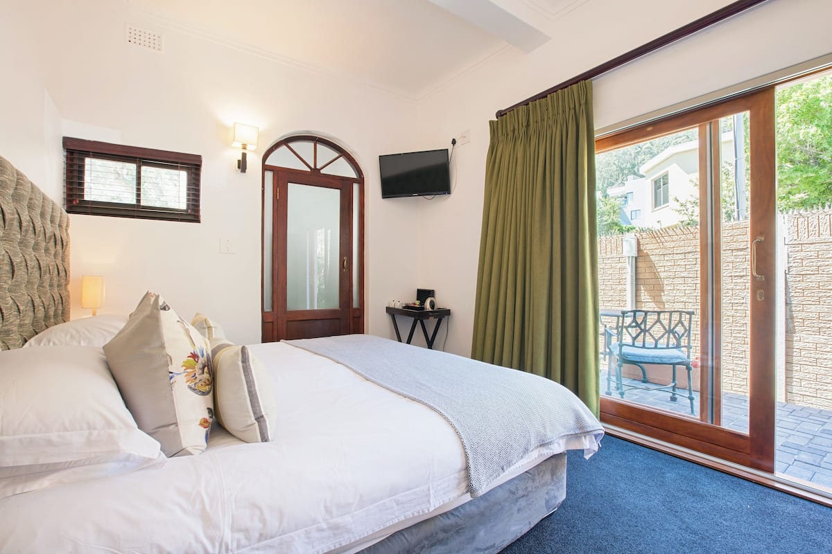Ein Schlafzimmer mit Bett, Fernseher, Fenster und Blick ins Freie.