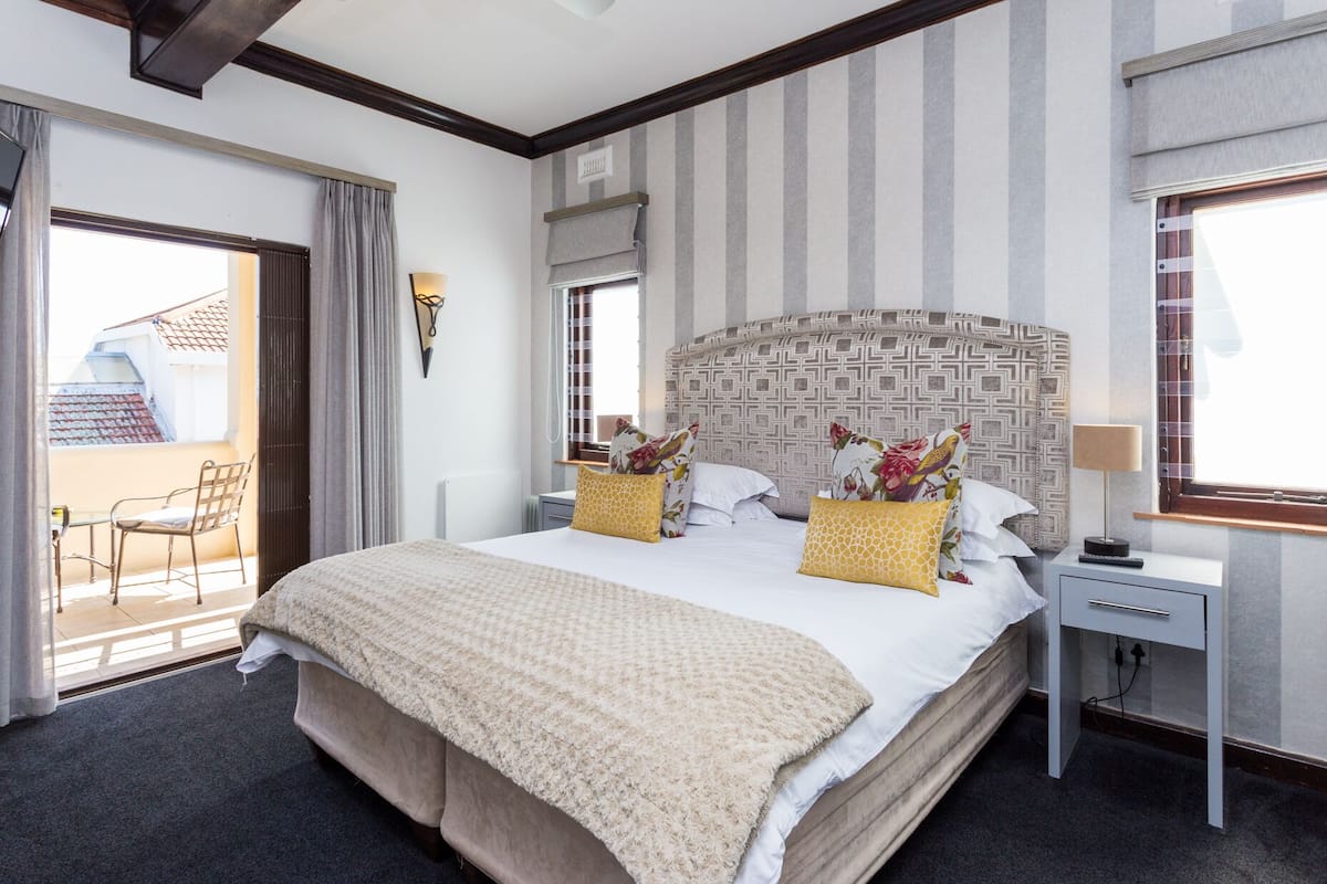 Ein Hotelzimmer mit einem großen Bett, einem Nachttisch, einem Sessel und einem Fenster mit Blick ins Freie.