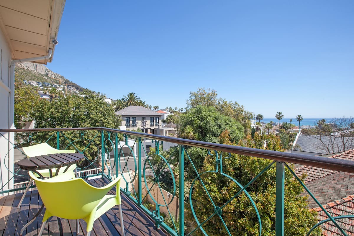 Ein Balkon mit Blick auf eine Hügelslandschaft, ein Gebäude und das Meer.