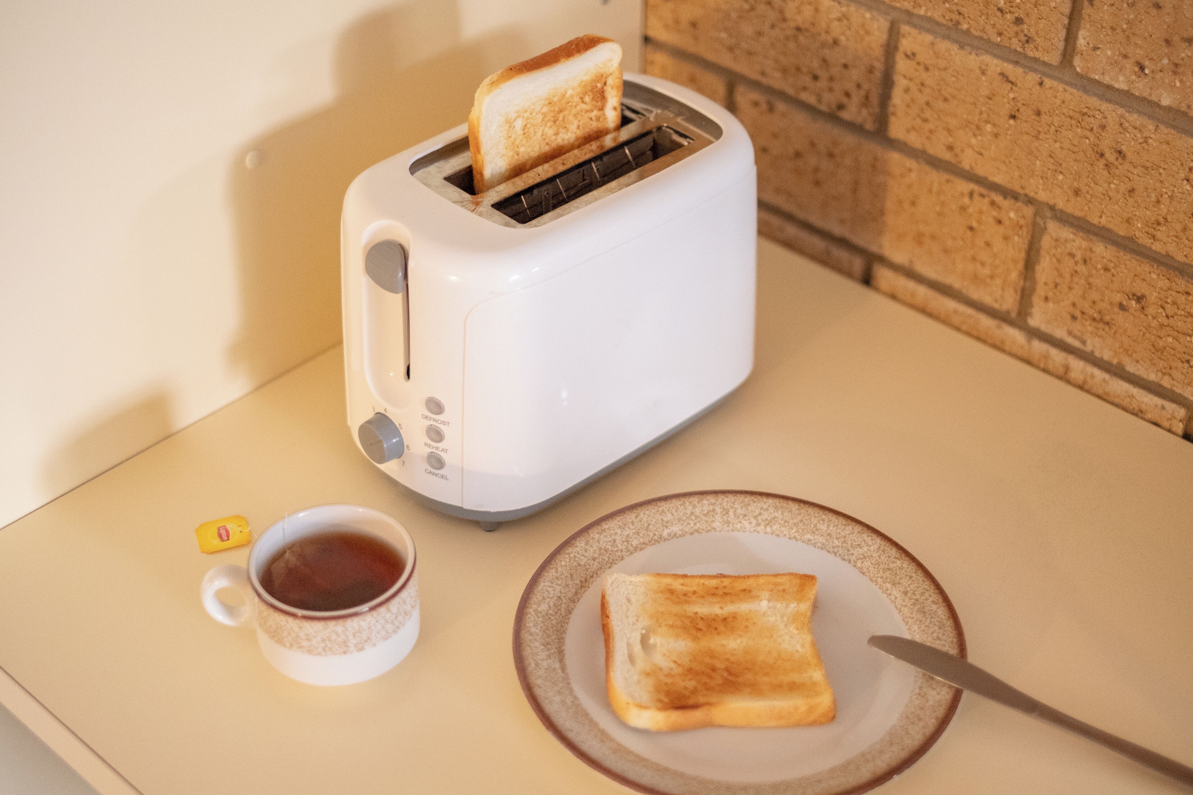 A toaster with a slice of toast on a plate, a cup of coffee, and a small yellow object on a table.
