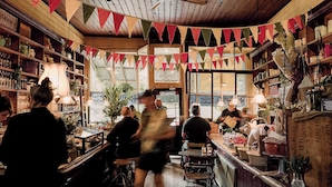 A cozy bar with wooden shelves and a rustic ceiling, featuring a variety of bottles and glassware.