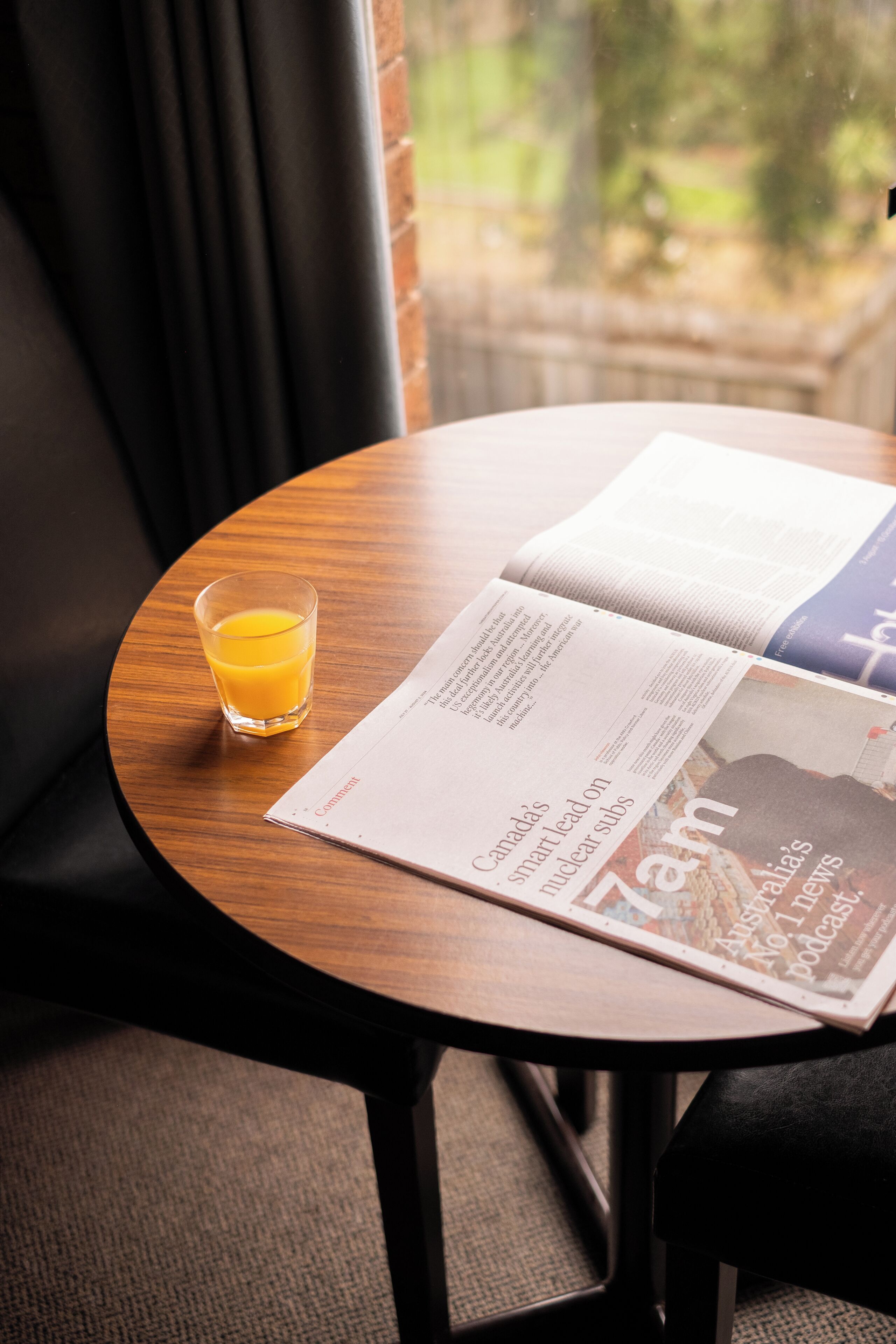 A round wooden table with a glass of orange juice and an open magazine.