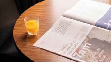 A round wooden table with a glass of orange juice and an open magazine.