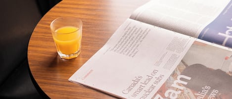 A round wooden table with a glass of orange juice and an open magazine.