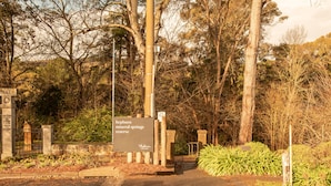 A sign for Hepburn Mineral Springs Reserve with a gate and pathway leading into a wooded area.
