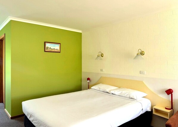 Habitación de hotel con una cama, dos lámparas de noche, una mesita de noche, un cuadro en la pared y un revestimiento de ladrillo.