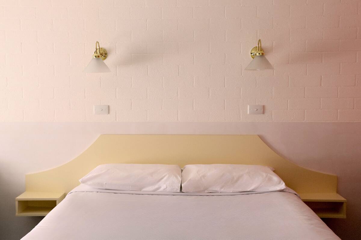 A bed with a wooden headboard, two bedside tables, and wall-mounted lamps.