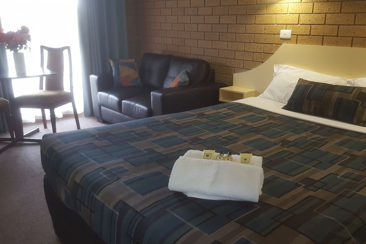 A hotel room with a bed, a chair, a nightstand, and a brick wall.