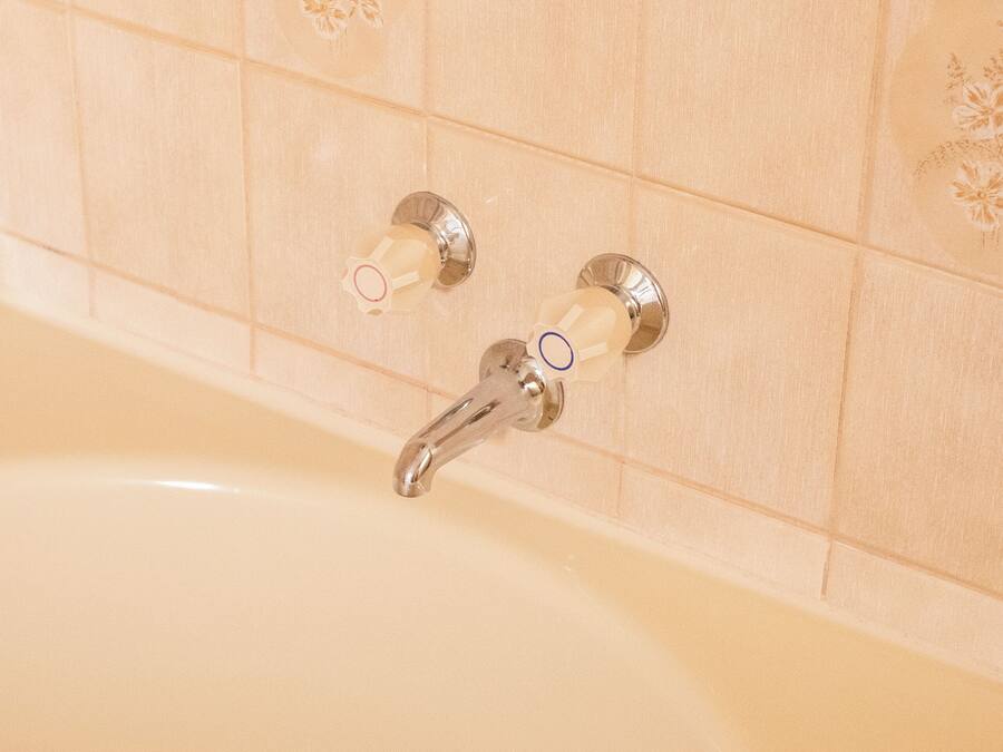 A bathtub with a chrome faucet and two soap dispensers mounted on the wall.