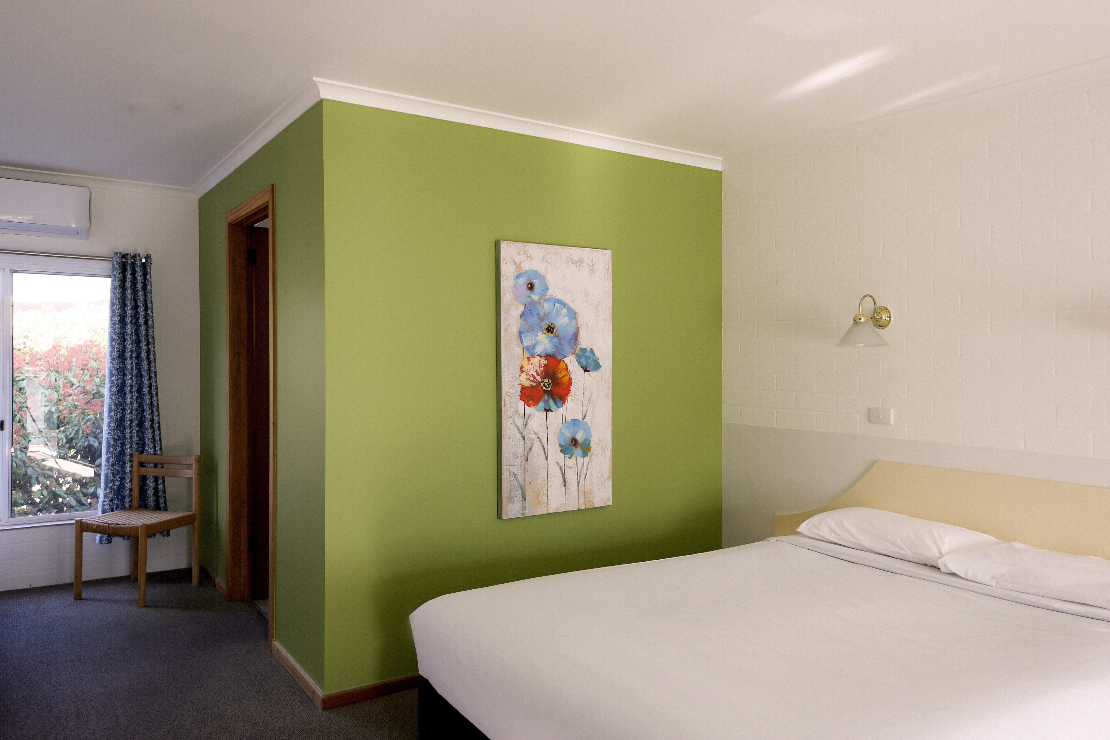 A hotel room with a bed, a chair, a painting on the wall, and a window with curtains.