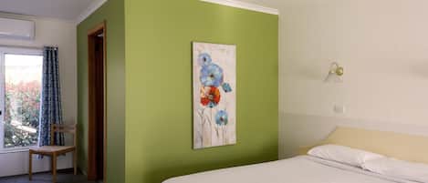 A hotel room with a bed, a chair, a painting on the wall, and a window with curtains.