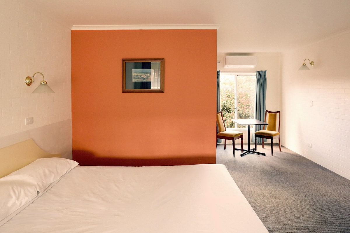 A hotel room with a large bed, a small table with chairs, and a window with curtains.