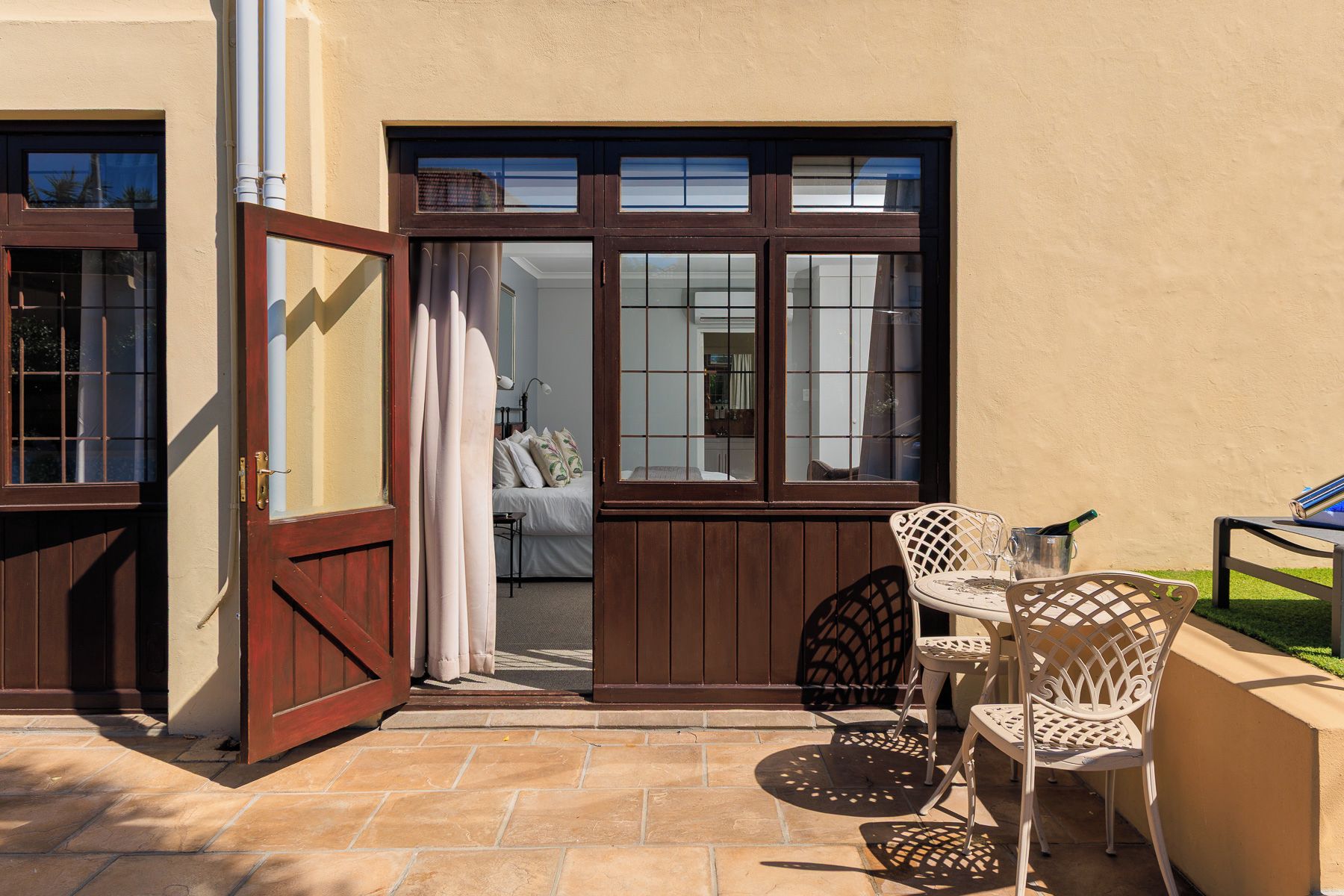 Un patio con una mesa y sillas, una puerta que da a un dormitorio y vistas al interior.