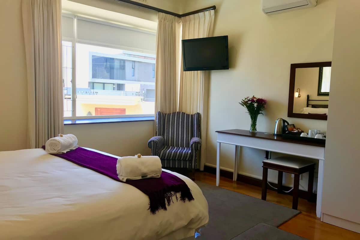 Hotellihuone, jossa on sänky, työpöytä, tuoli, televisio ja ikkuna, jossa on verhot.