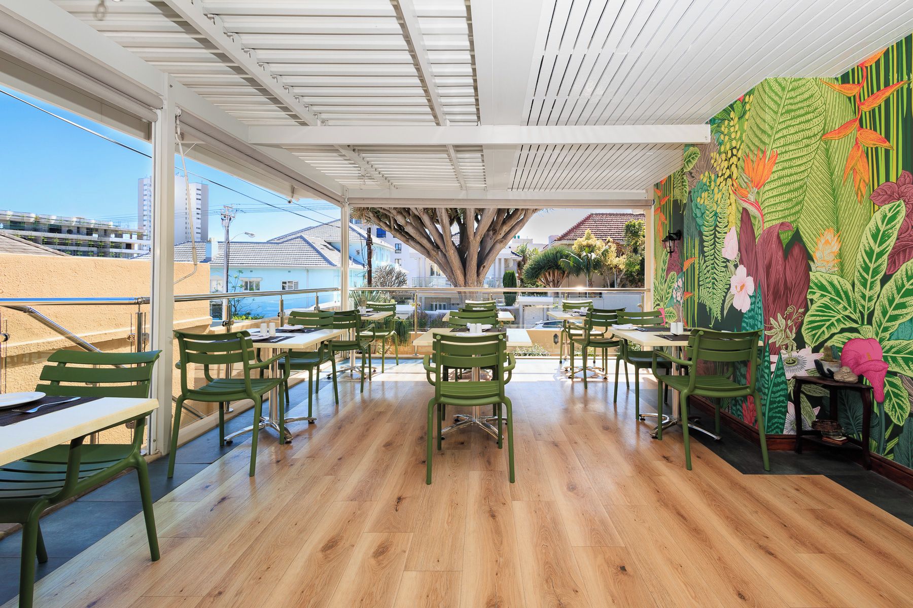 An outdoor dining area with wooden flooring, green chairs, and tables.