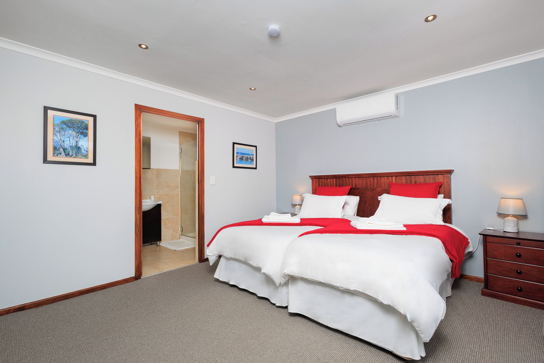 Habitación de hotel con cama, mesita de noche, lámpara, un cuadro en la pared y una puerta que da a un baño.