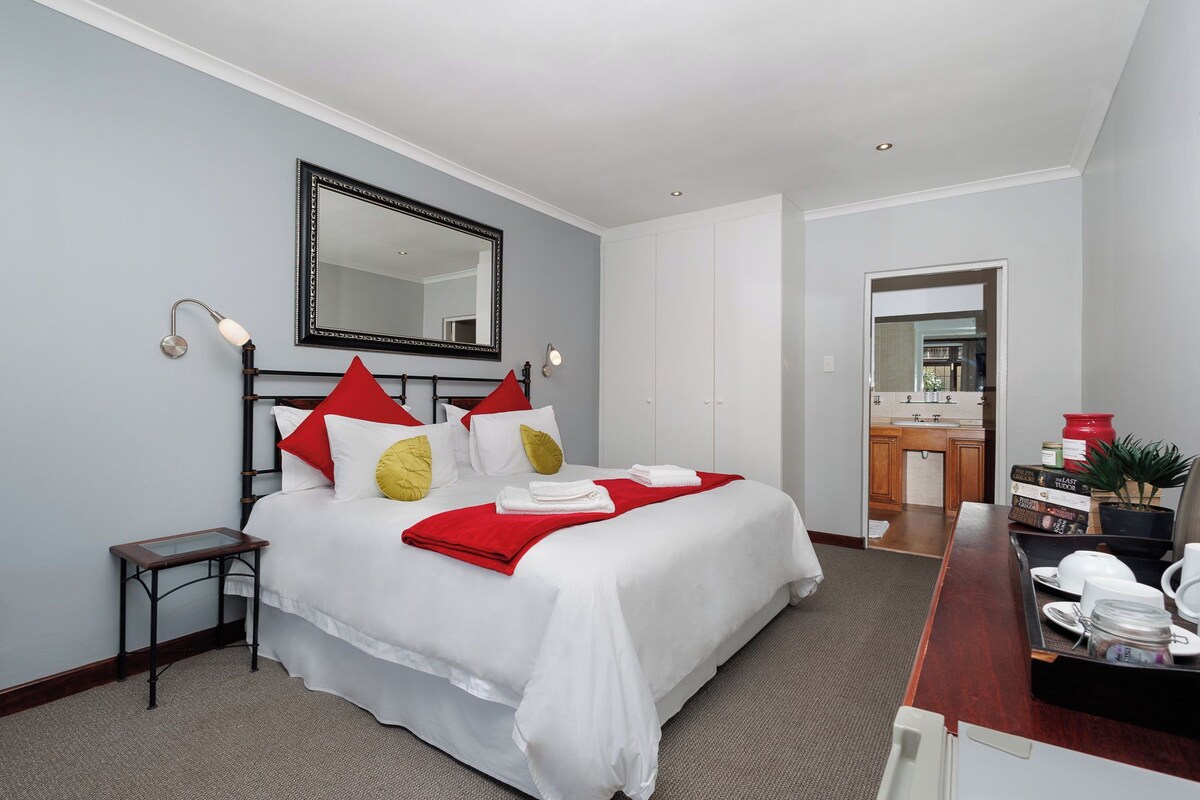 Habitación de hotel con cama, mesita de noche, espejo y vista al baño.