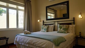 A neatly made bed with a green throw blanket, a large mirror above it, and two bedside lamps. - Sundown Manor Guest House (Cape Town)