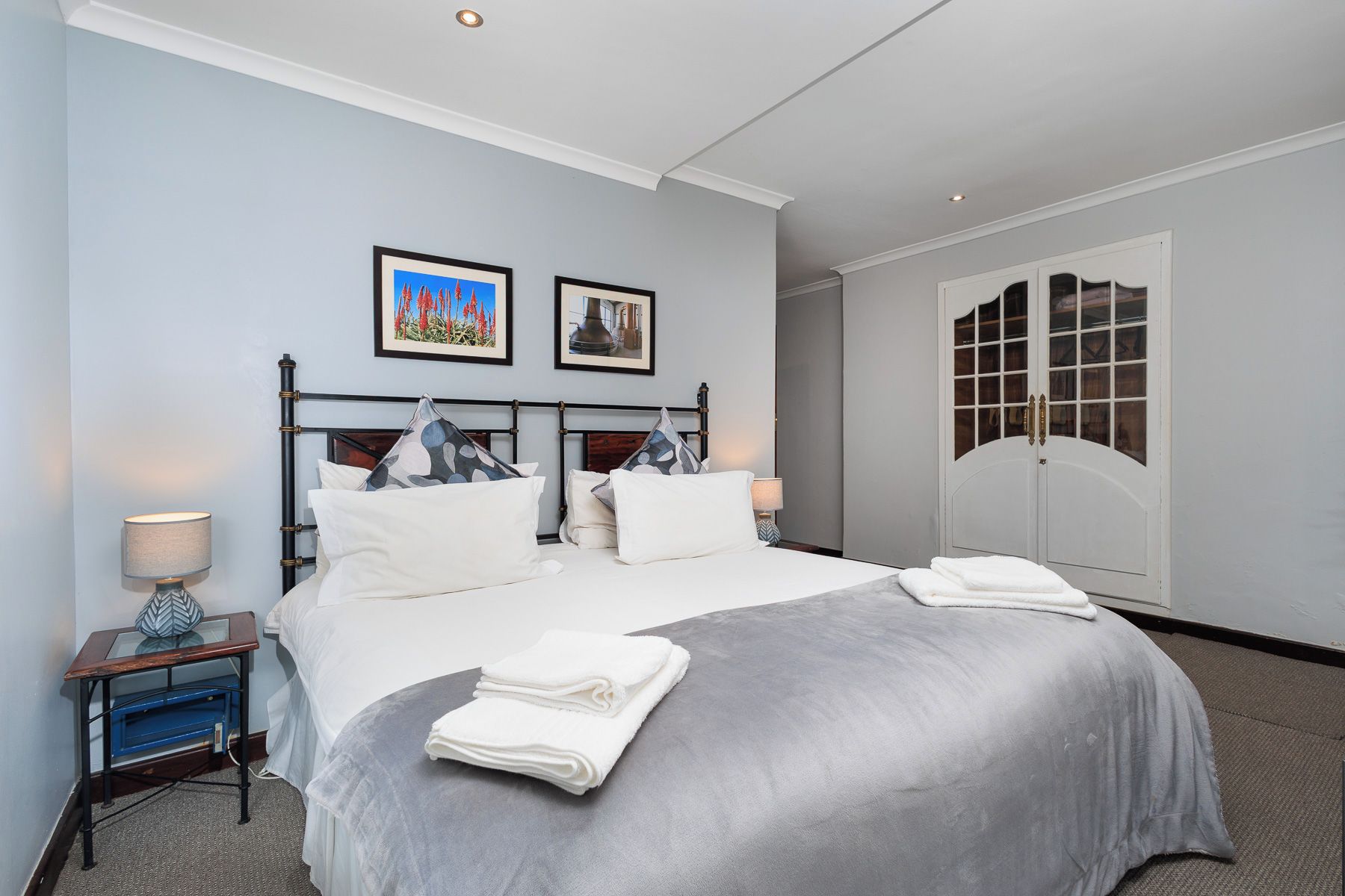Habitación de hotel con cama, dos cuadros en la pared, un armario y una mesita de noche con lámpara.