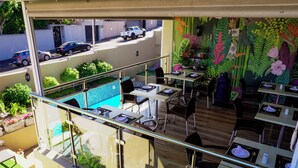 A rooftop dining area with a pool view, outdoor seating, and a mural of tropical plants. - Sundown Manor Guest House (Cape Town)