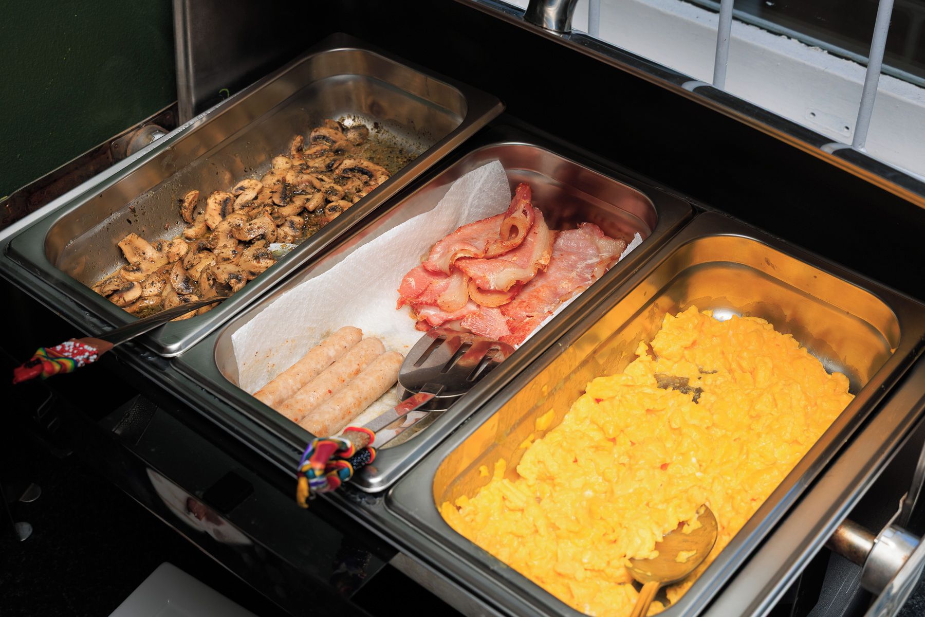 A buffet with various food options including scrambled eggs, bacon, and chicken.