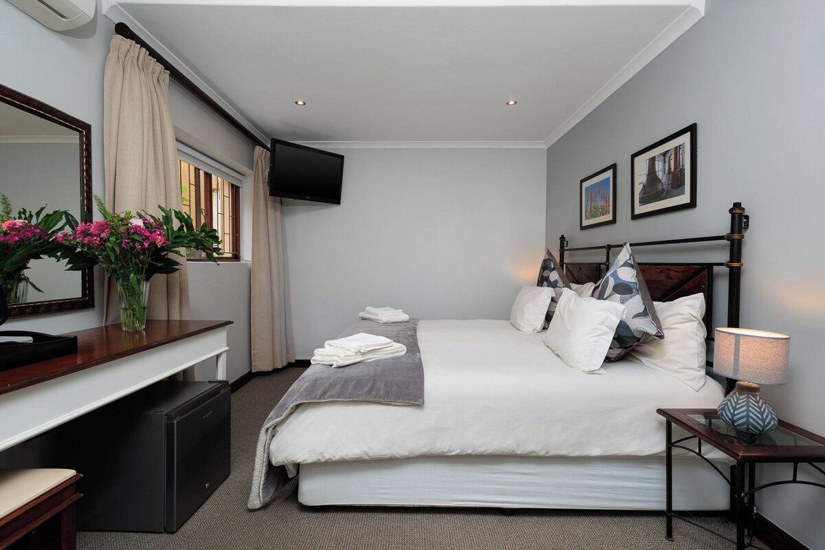 Habitación de hotel con cama, mesita de noche, escritorio, silla, televisión y obras de arte en las paredes.