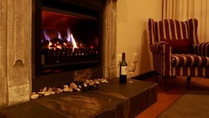 A fireplace with burning logs, a bottle of wine, and a glass on a stone ledge. - Sundown Manor Guest House (Cape Town)
