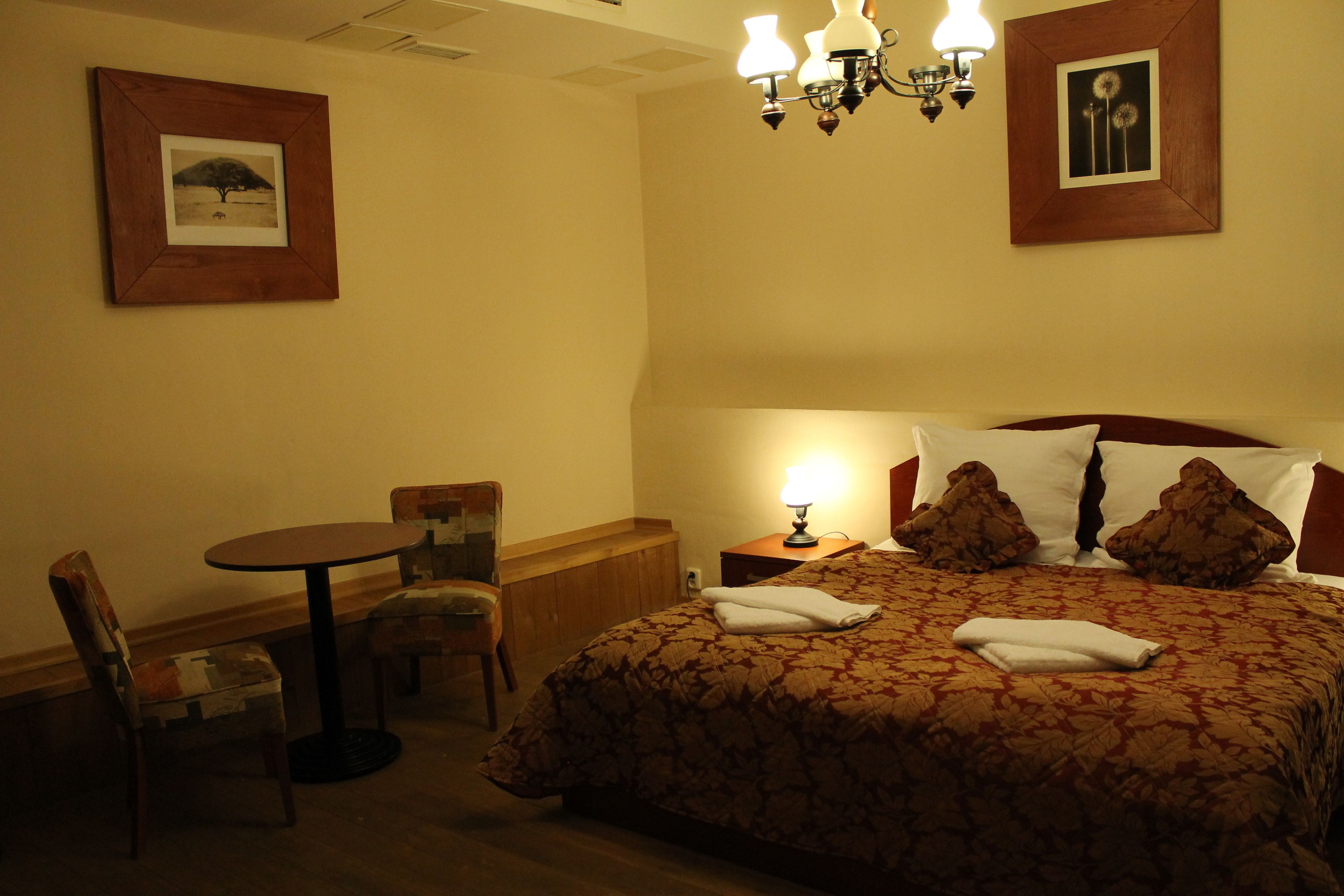 A hotel room with a bed, a round table, a chair, and a nightstand with a lamp.
