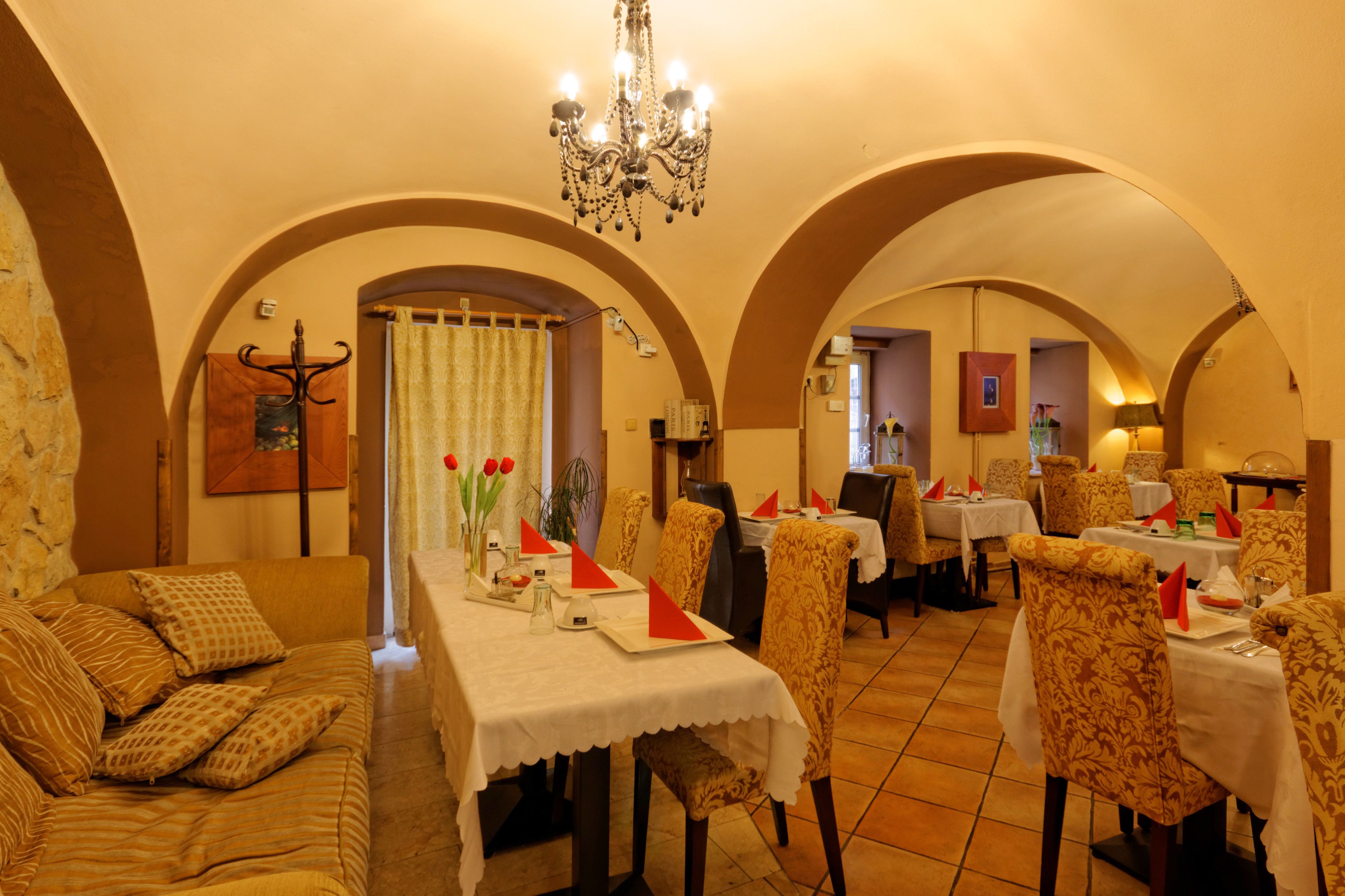Un comedor con mesas dispuestas para dos, techos abovedados y un candelabro.