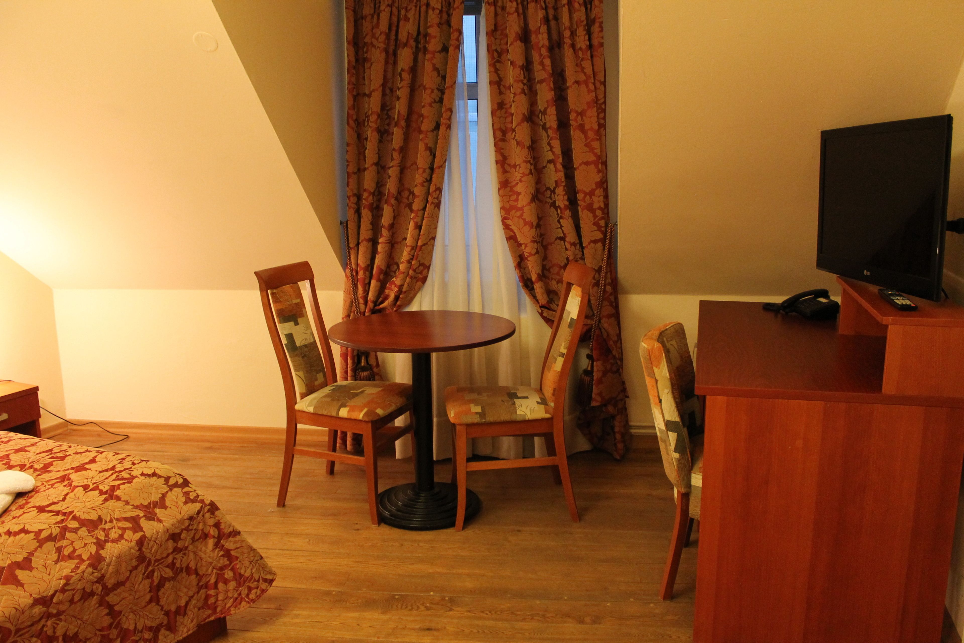 Una habitación de hotel con cama, una mesa redonda con sillas, televisión y cortinas.