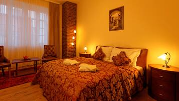 A hotel room with a large bed, a wooden nightstand, a chair, a small table, and a large window with curtains.