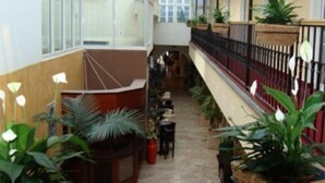 A high-ceilinged indoor corridor with potted plants, tables, and chairs along the sides, suggesting a public space within a building. - Enjoy Inn (Plzen)