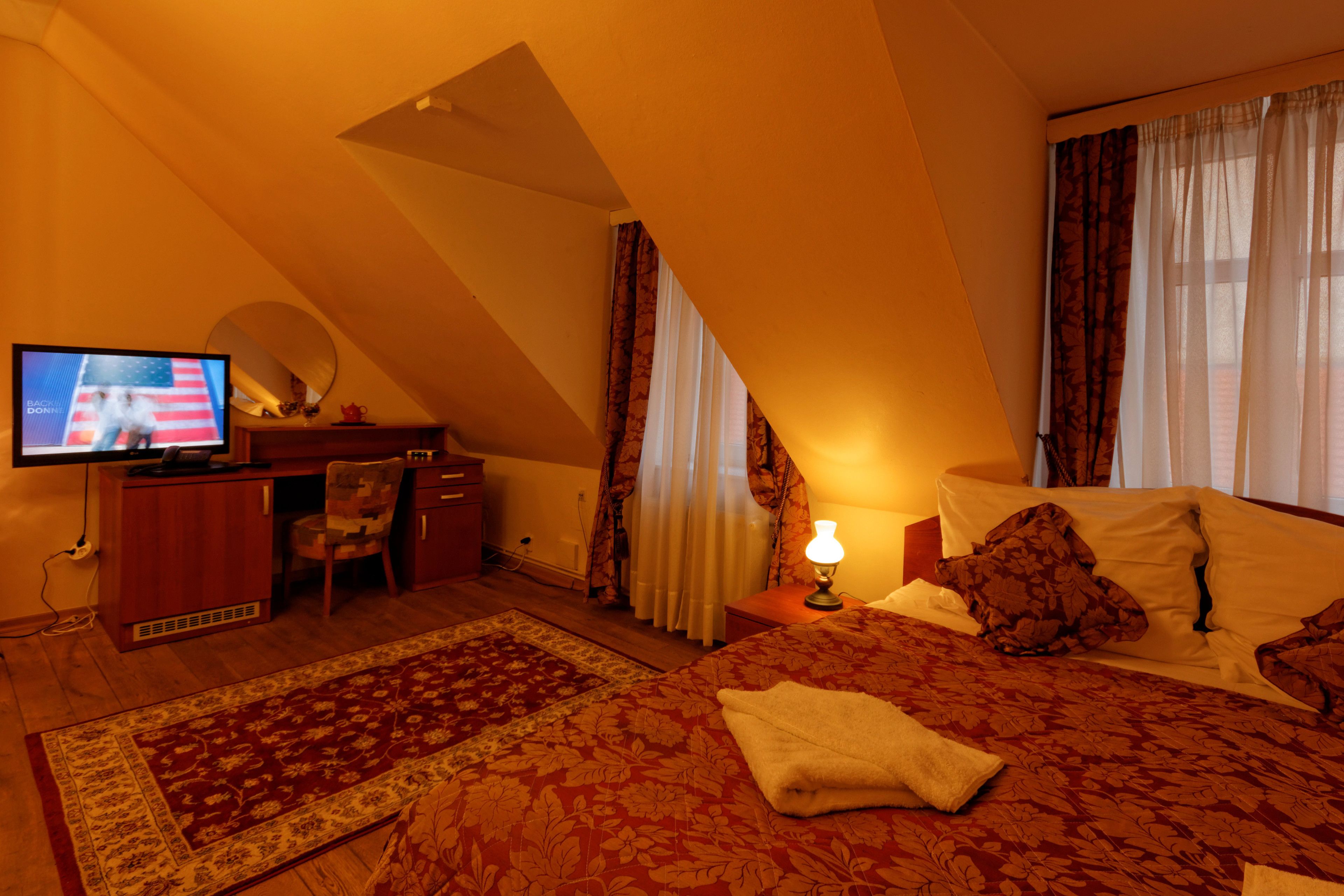Een hotelkamer met een bed, een bureau met een televisie, een stoel, een bureaulamp en gordijnen.