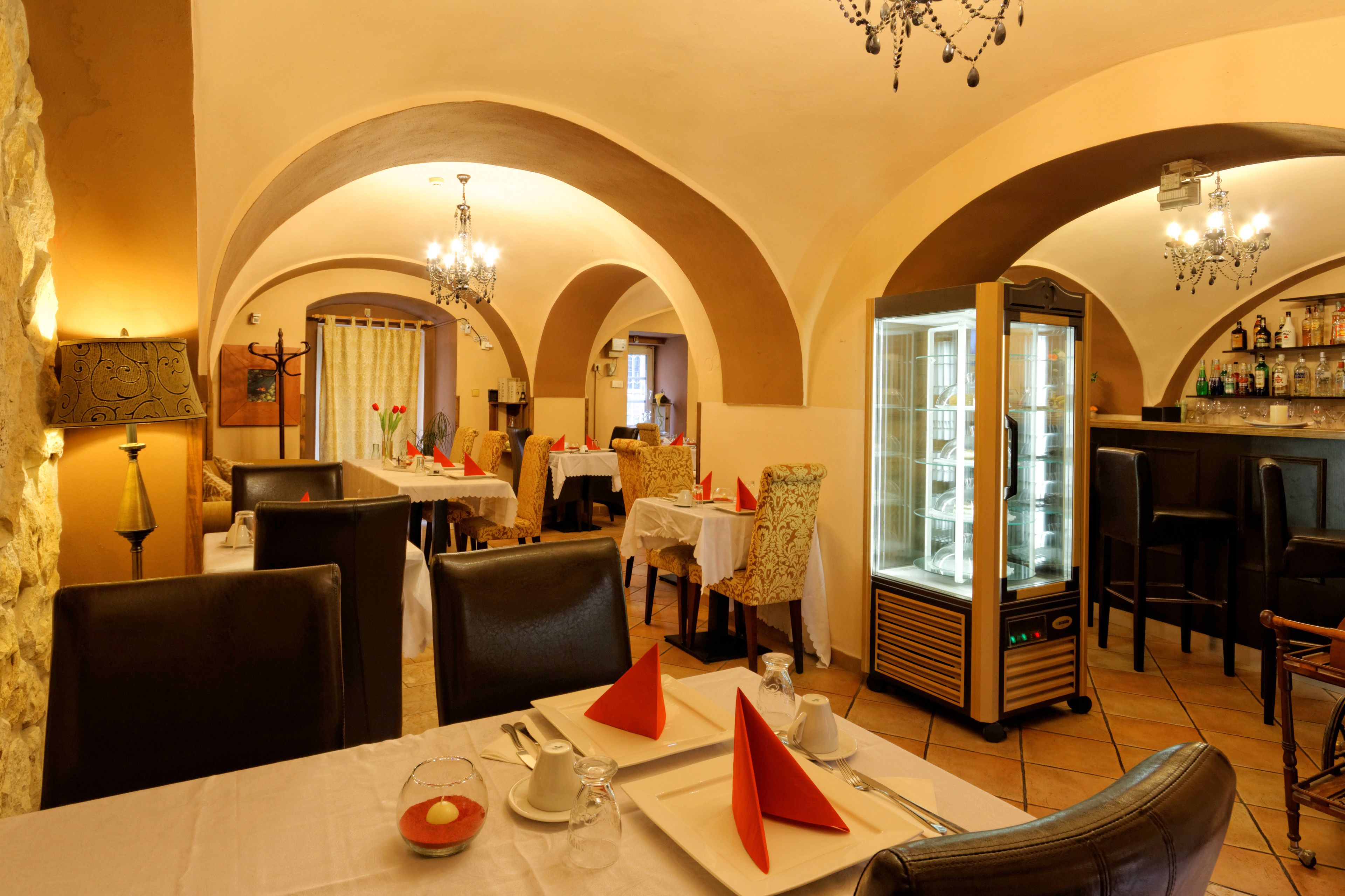 Un restaurante con techos abovedados, una zona de bar y un minibar. Las mesas están dispuestas con servilletas rojas y manteles blancos.
