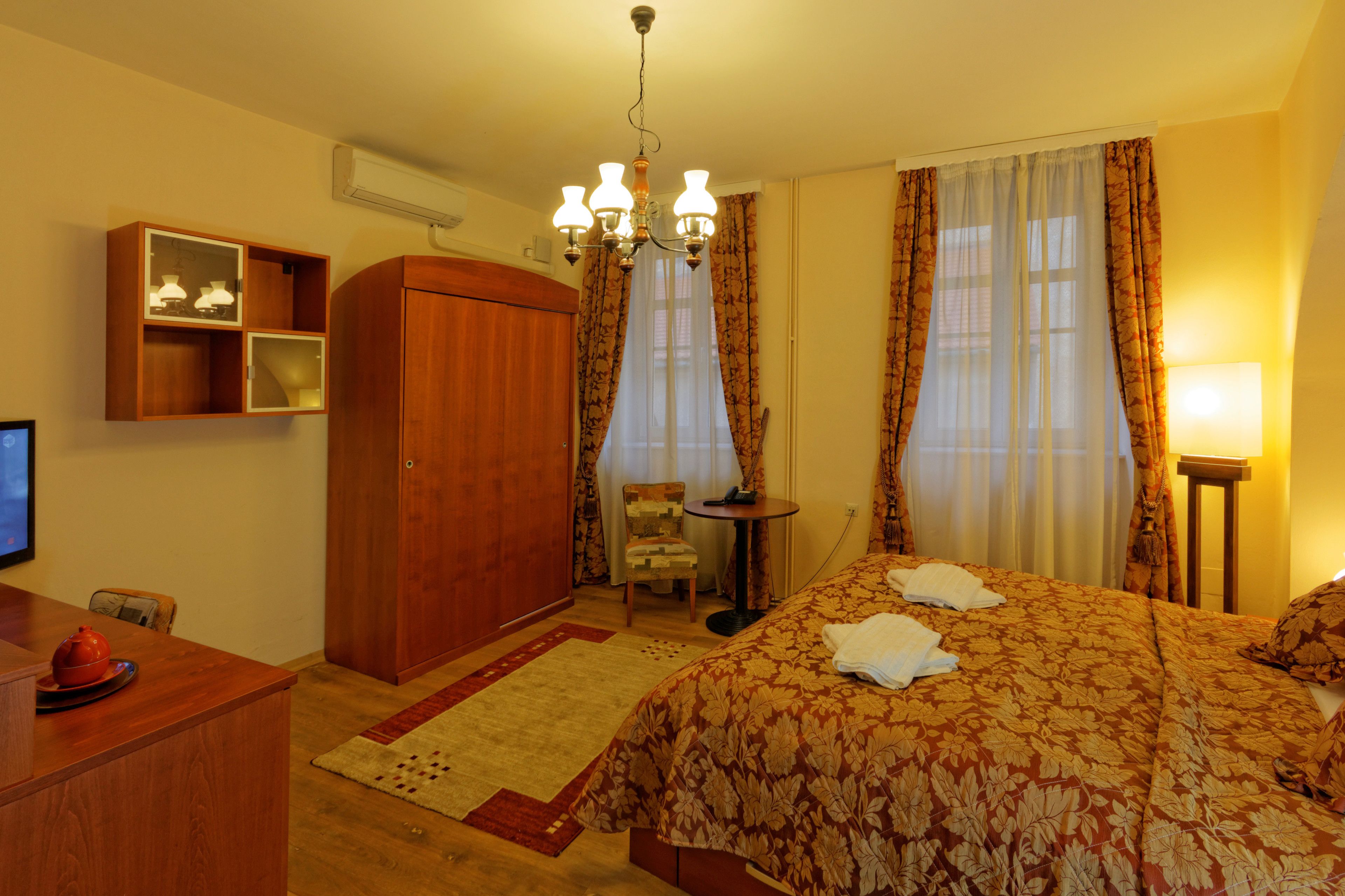 A hotel room with a bed, a desk, a wardrobe, a chair, a small table, and a lamp.