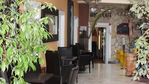 A hotel lobby with a dining area, multiple chairs, a staircase, and potted plants. - Enjoy Inn (Plzen)