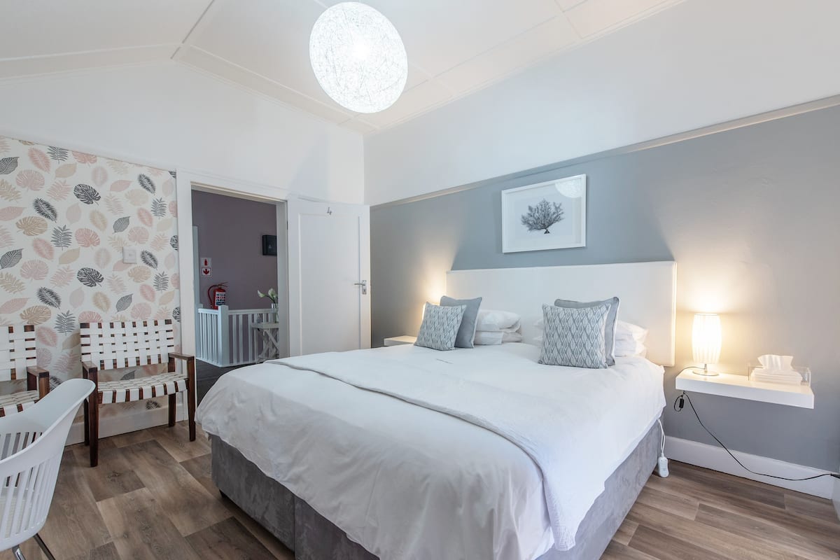 Een slaapkamer met een groot bed, een nachtkastje met een lamp, een stoel en een muur met behang met bladmotieven.