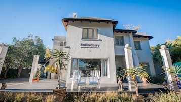 Un edificio a due piani chiamato "Ballinderry The Robertson Guest House" con un patio arredato con poltrone Adirondack bianche e piante in vaso.