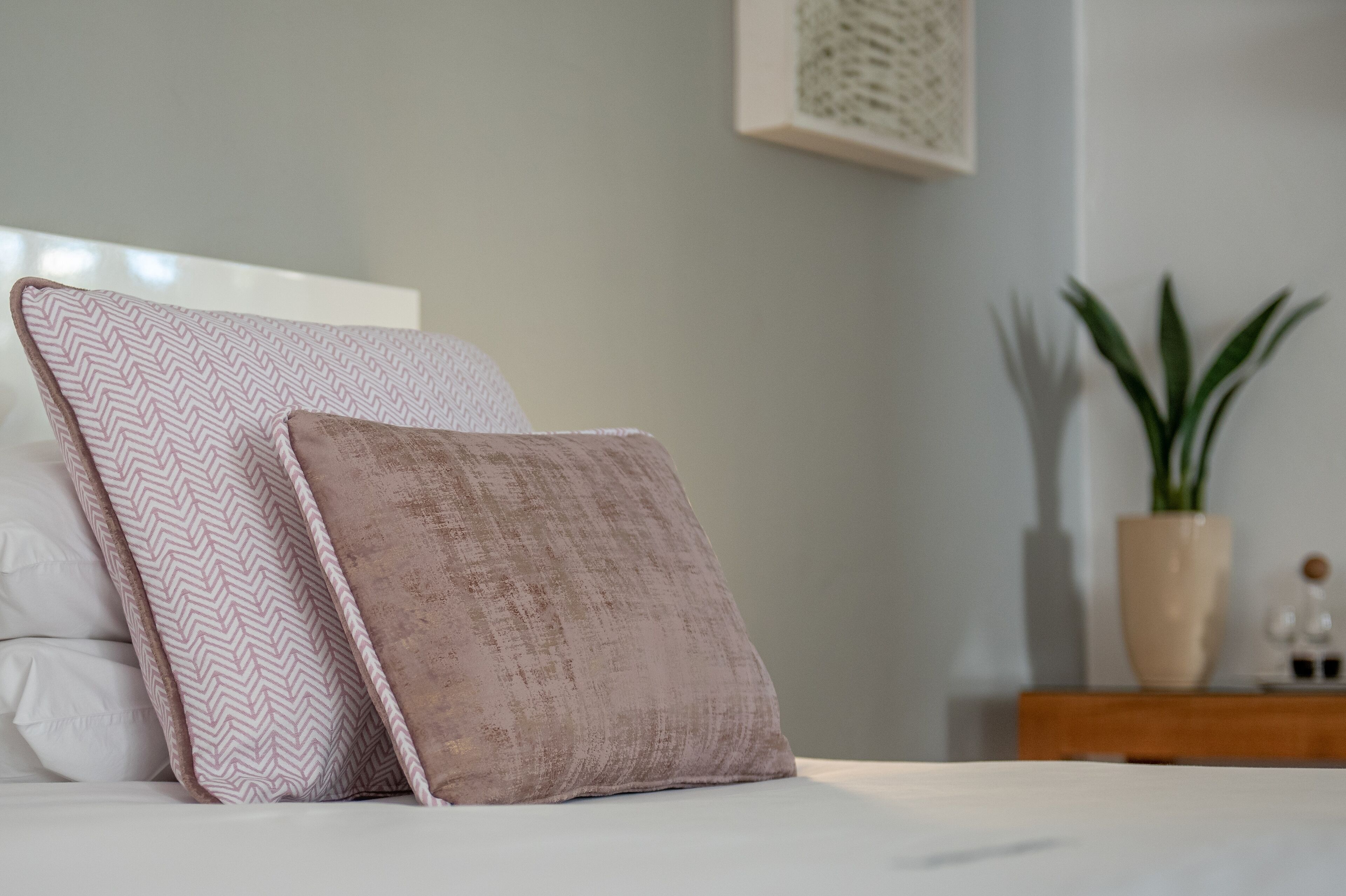 A bed with two pillows, a nightstand with a plant, and a framed picture on the wall.