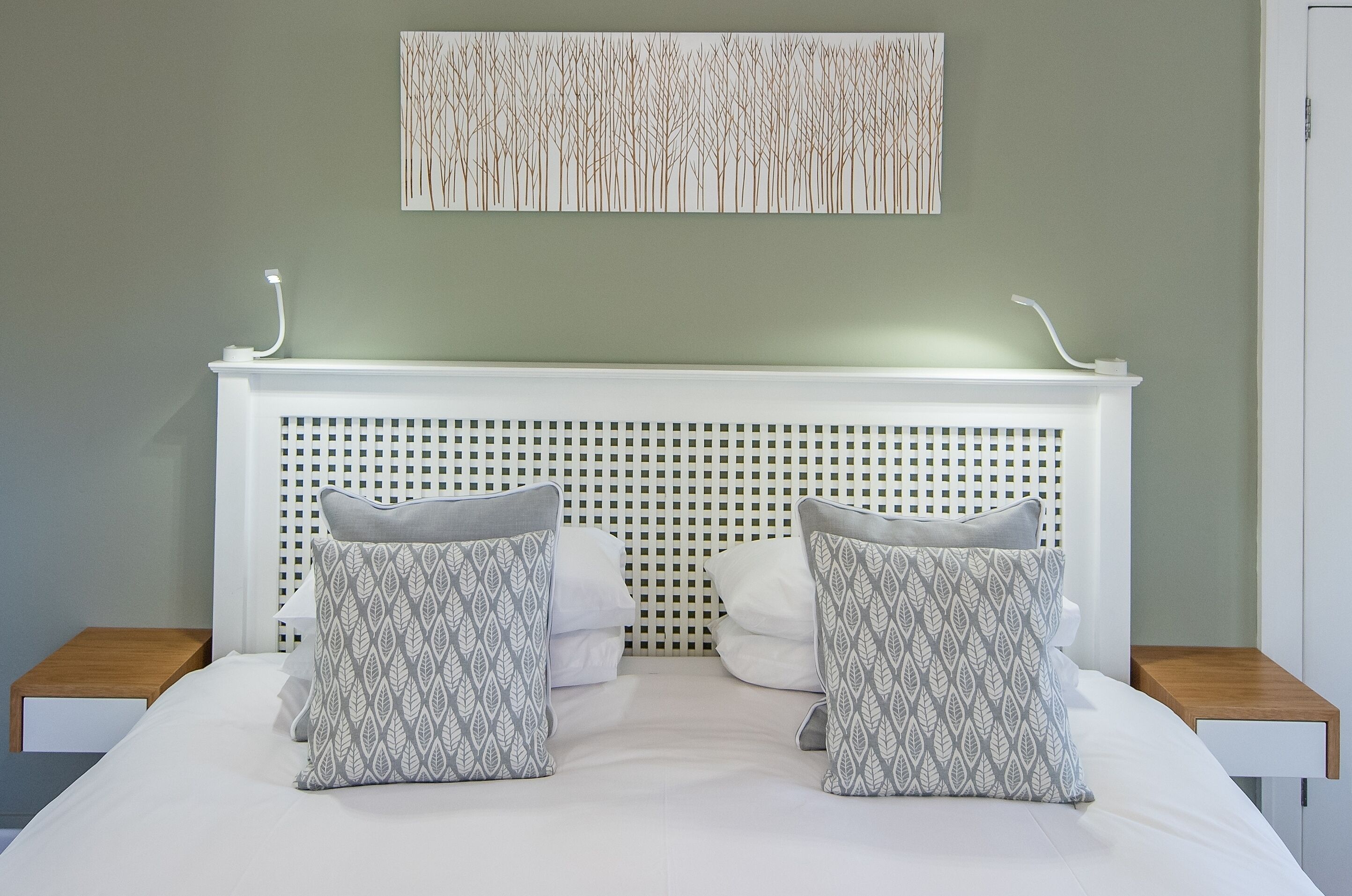 A neatly made bed with a white headboard, two pillows with a leaf pattern, and a wall-mounted light fixture.