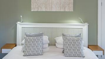 A neatly made bed with a white headboard, two pillows with a leaf pattern, and a wall-mounted light fixture.